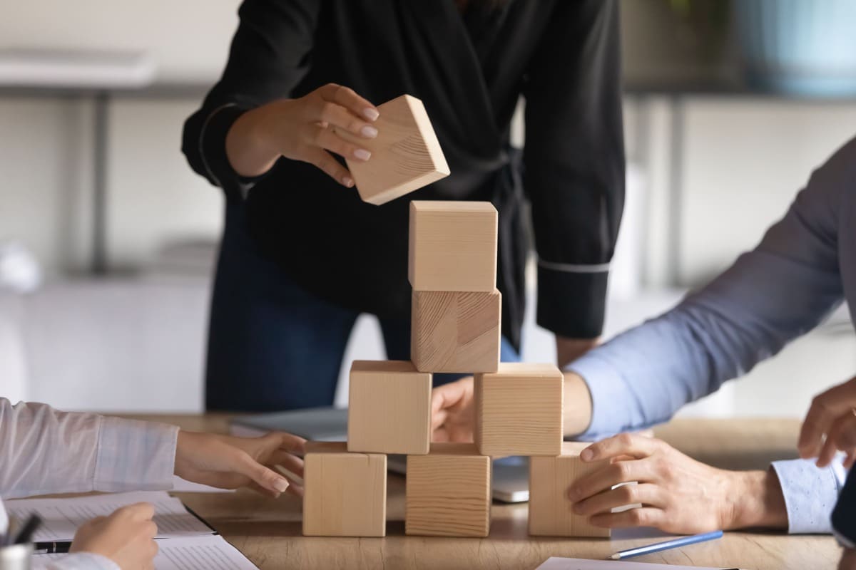 Angajați construind împreună un turn din cuburi de lemn